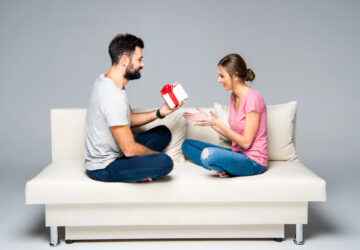 A man exchanging a gift with a woman seated on a white couch.
